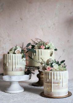 three cakes with white frosting and flowers on top are sitting on a table next to each other