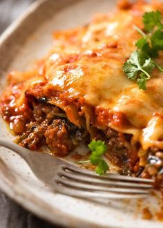 a white plate topped with lasagna covered in sauce and cheese next to a fork