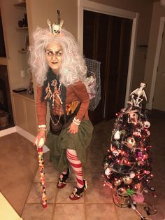 an old woman dressed in costume sitting next to a christmas tree with decorations on it