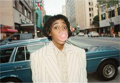 a man in a suit blowing a bubble out of his mouth while standing next to a car