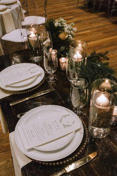 the table is set with white plates and silverware, gold rimmed glasses and candles