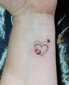 a small tattoo on the wrist of a woman with a rose and hearts in it