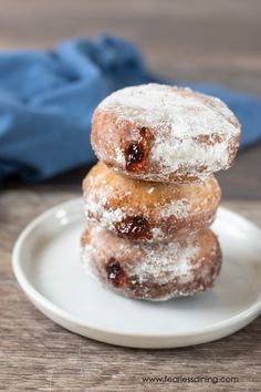 three donuts stacked on top of each other on a white plate with powdered sugar