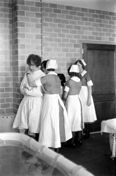 several women in nurses uniforms are standing by a brick wall and looking at something on the floor