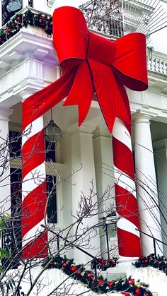 a large red and white striped bow on the side of a building with christmas decorations around it