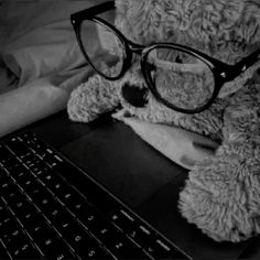 a teddy bear wearing glasses sitting in front of a laptop computer with its head resting on the keyboard