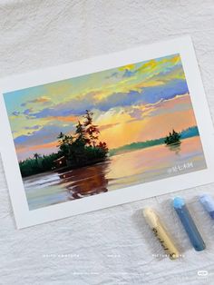 three markers are next to a painting of a sunset on the water with trees in the distance