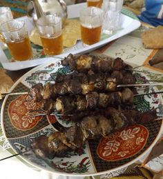 a plate full of skewers of food on a table next to glasses of beer