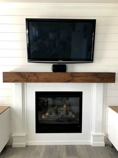 a flat screen tv mounted above a fireplace in a living room with white walls and wood flooring