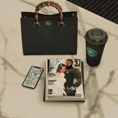 a magazine, cell phone and cup sitting on top of a table next to a bag