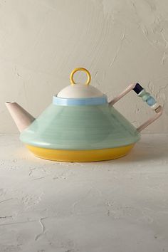 a ceramic teapot with two handles sitting on top of a white table next to a wall