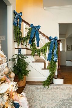 christmas decorations on the banisters and stairs in a house with blue bows hanging from them