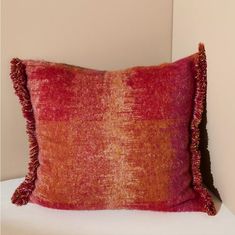 an orange and red pillow sitting on top of a white bed next to a wall