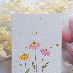 a card with flowers painted on it next to a teddy bear and some pink feathers