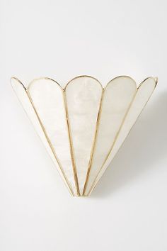 a white and gold fan shaped brooch on a white surface with no one around it