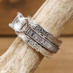 two wedding bands with an intricate design and a princess cut diamond in the center, sitting on top of a piece of wood