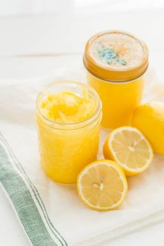 two jars filled with lemon curd next to sliced lemons on a white towel