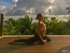 a woman is doing yoga on a deck overlooking the ocean and trees in the background