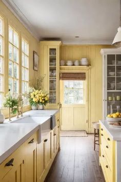 a kitchen with yellow cabinets and white counter tops in front of a window filled with sunflowers