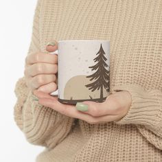 a woman holding a coffee mug in her hands with trees painted on the front and sides