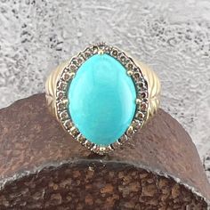 a turquoise stone ring sitting on top of a piece of wood in front of a wall