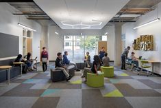 people are sitting and standing in an open room with colorful carpeting on the floor