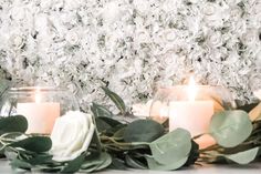 candles are lit in front of flowers and greenery