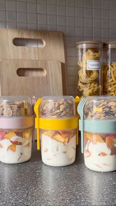 four containers with food in them sitting on a counter top next to some bowls and utensils