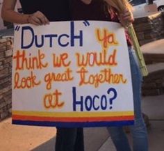 two women holding a sign that says dutch you think we would look great together at hoco?