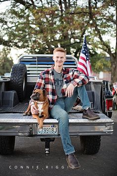 a man sitting on the back of a pickup truck with his dog and american flag