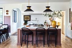 a kitchen with wooden flooring and black bar stools next to an island in the middle