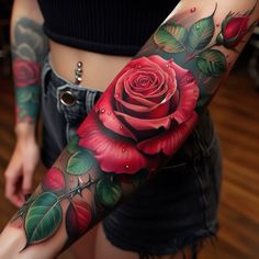 a woman's arm covered in tattoos with roses and leaves on the forearm, behind her is a red rose