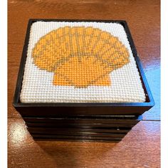 a cross stitch box with an orange seashell on it's lid sitting on top of a wooden table