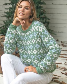 a woman sitting on a bench in front of a christmas tree wearing a green and white sweater