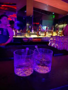 two glasses filled with water sitting on top of a bar