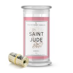 a pink candle next to a roll of money on a white background with the words saint jude written in gold