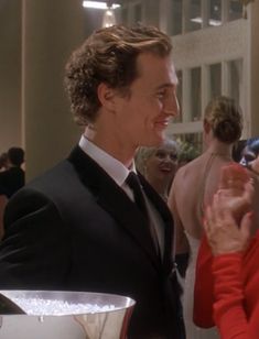 a man in a tuxedo talking to a woman in a red dress at an event