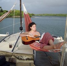 a woman sitting in a hammock on top of a boat playing the guitar