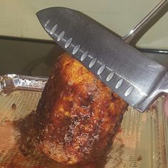 a person holding a large knife over a piece of meat on top of a pan