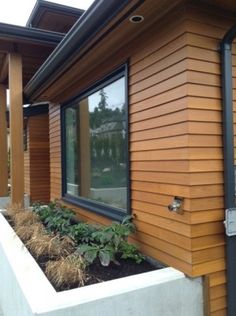 an outside view of a house with wood siding and plants growing in the planter