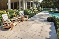 two lawn chairs sitting on top of a stone patio next to a swimming pool in front of a house