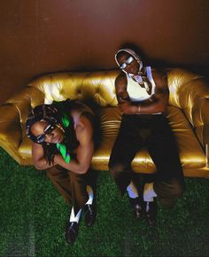 two people sitting on top of a couch in front of a brown wall and green grass