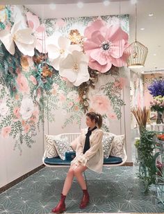 a woman sitting on a bench in front of a wall with paper flowers hanging from it