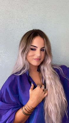 a woman with blonde hair wearing a purple shirt and holding her hand up to her chest