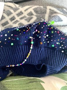 a blue sweater with colorful beads on it sitting on a bed next to a remote control