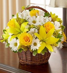 a basket filled with yellow and white flowers on top of a wooden table next to a lamp