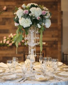 a tall vase with flowers on top of a table set for a formal dinner party