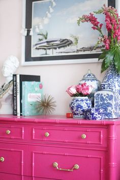 a pink dresser with blue and white vases on it's top next to a painting