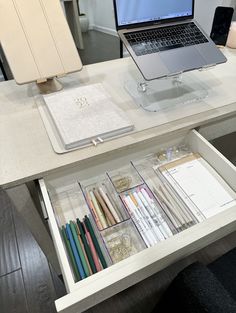 an open laptop computer sitting on top of a white desk next to a drawer filled with papers