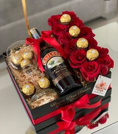 a wine bottle and chocolates in a gift box with red roses on the table